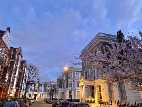 une rue de la ville avec des bâtiments et un arbre à fleurs dans l'établissement Modern flat & balcony in historic West Kensington, à Londres