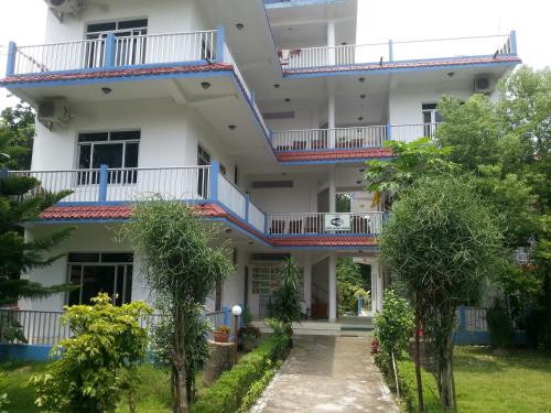 a white building with blue balconies and trees at Hotel Shiva's Dream in Sauraha