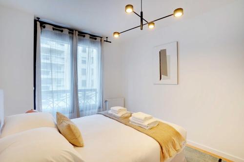 Schlafzimmer mit einem Bett mit weißer Bettwäsche und einem Fenster in der Unterkunft Raffinement et Confort dans cette Résidence à Levallois-Perret in Levallois-Perret