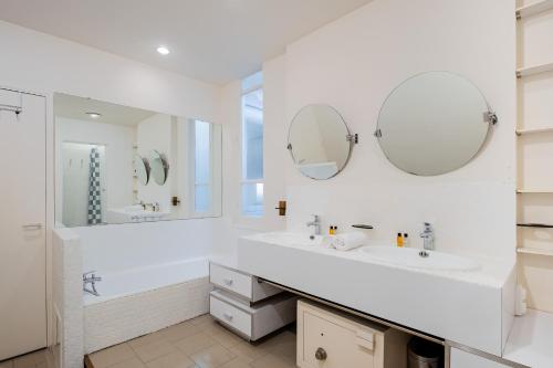 La salle de bains blanche est pourvue de deux lavabos et de miroirs. dans l'établissement Veeve - Clichy Couture, à Paris