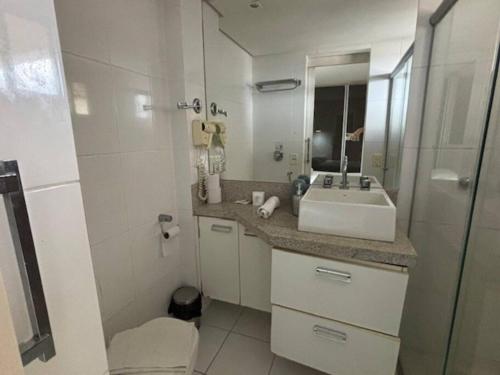La salle de bains blanche est pourvue d'un lavabo et d'un miroir. dans l'établissement Flat Apart Bristol Hotel Goiânia - Crystal Place, à Goiânia