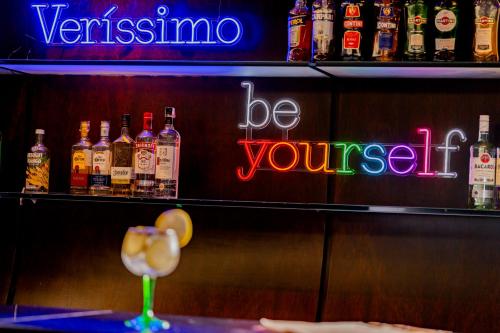 a bar with bottles of alcohol and a neon sign at Pergamon SP Frei Caneca by Accor in Sao Paulo
