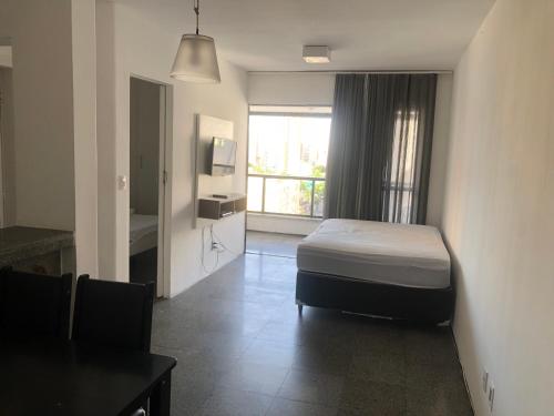 a bedroom with a bed and a table and a window at Via Venetto Flat Temporada in Fortaleza