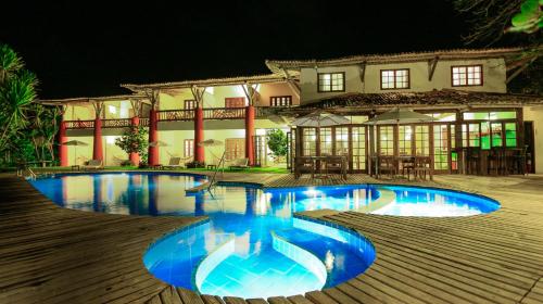 a swimming pool in front of a house at night at Pousada Farol das Tartarugas in Praia do Forte