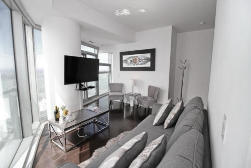 a living room with a couch and a flat screen tv at Presidential 2+1BR Condo, Entertainment District (Downtown) w/ CN Tower View, Balcony, Pool & Hot Tub in Toronto