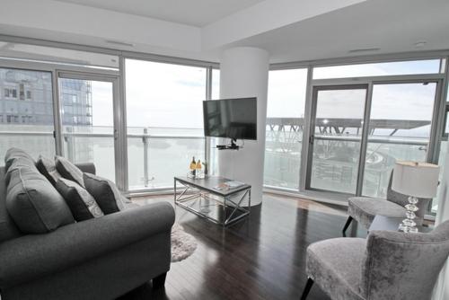 a living room with a couch and chairs and a television at Presidential 2+1BR Condo, Entertainment District (Downtown) w/ CN Tower View, Balcony, Pool & Hot Tub in Toronto