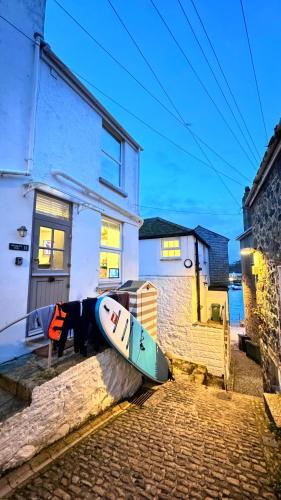 a surfboard sitting on the side of a house at "SMUGGLERS HIDE" & "SMUGGLERS CABIN" - A 2 Bedroom FISHERMANS COTTAGE with Childs Bunk and HARBOUR VIEWS - and also a private entrance connecting 1 BED STUDIO - 10 Metres To Sea Front - 2023 GLOBAL REFURBISHMENT AWARD WINNER in St Ives