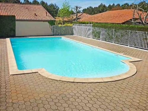 a large blue swimming pool in a backyard with a fence at Chaleureuse maisonnette avec piscine partagée in Capbreton