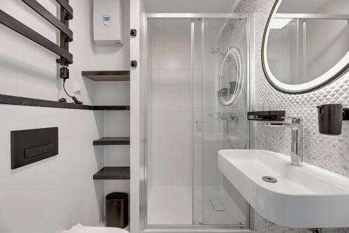 a white bathroom with a sink and a shower at Petit Repit by Grand Apartments in Sopot