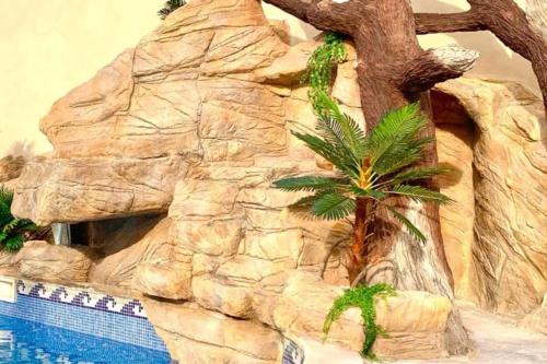 een rotswand met een palmboom naast een zwembad bij Villa 4P piscine avec toboggan et cascade in Bessan