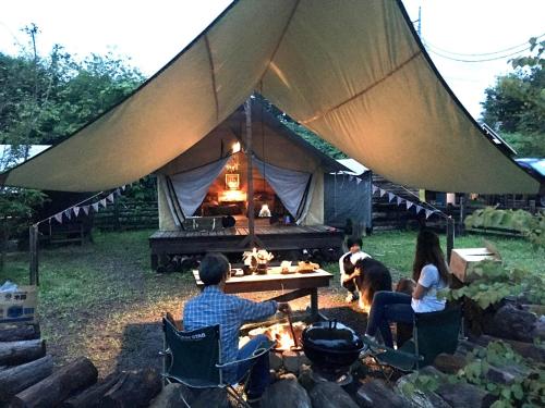 Un gruppo di persone seduti intorno al fuoco di fronte a una tenda di Camp inn Kiyosato GRANDEUR - Vacation STAY 42080v a Hokuto