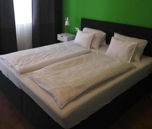 a large bed with white sheets and a green wall at DOMS Gästehaus in Frauenkirchen