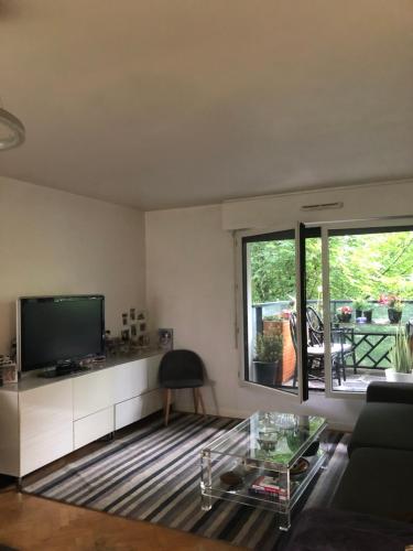 ein Wohnzimmer mit einem TV und einem Glastisch in der Unterkunft JO 2024 Bel APPARTEMENT DANS UN ECO QUARTIER ANIME PROCHE METRO TRAM ET TOUR EIFFEL in Boulogne-Billancourt