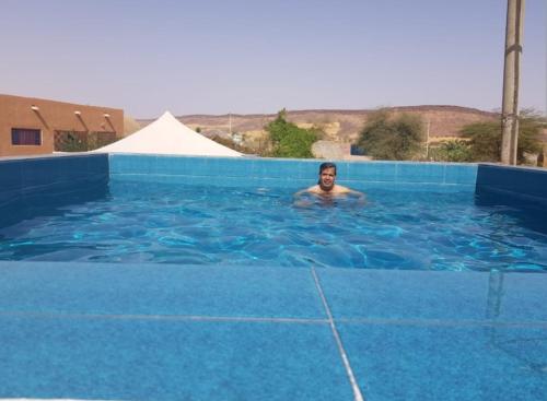 a man swimming in a blue swimming pool at Camping-Auberge Odette du Puigaudeau et Aziza in Atar