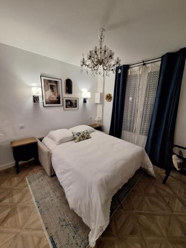 - une chambre avec un grand lit blanc et un lustre dans l'établissement L'Annexe de MaLou, à Maisons-Laffitte