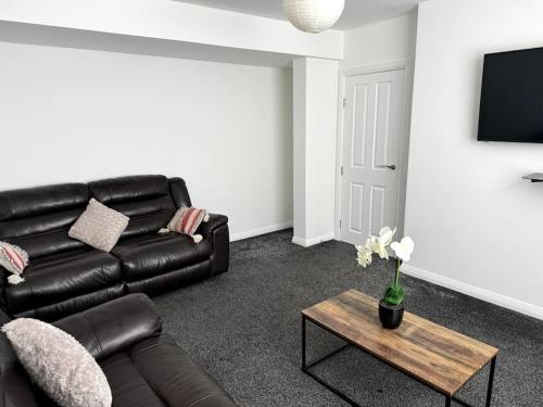 a living room with a black leather couch and a table at Entire 6 bedroom house in Oldham in Moston