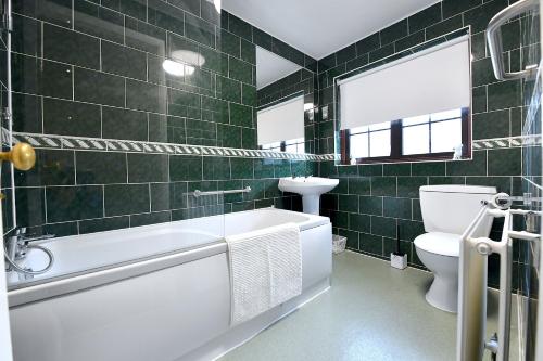 a green tiled bathroom with a tub and a toilet at Large home near central London in London