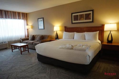 a hotel room with a large bed and a couch at Ramada by Wyndham Kelowna Hotel & Conference Center in Kelowna
