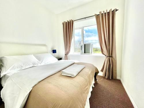 a white bedroom with a bed and a window at Clydfan in Holyhead