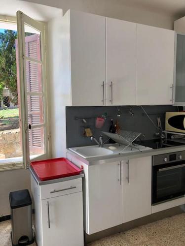 une cuisine avec des armoires blanches, un évier et une fenêtre dans l'établissement Charmant logement sur la plage, à Serra-di-Ferro