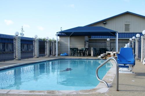 a swimming pool with a blue chair and an umbrella at Lone Star Inn Llano in Llano