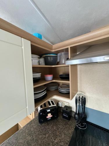 a kitchen cabinet with plates and utensils in it at 6 Berth Static Caravan, Golden Palm Resort, Chapel St Leonard's in Chapel Saint Leonards