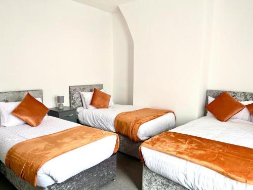 Pokój z 3 łóżkami i pomarańczowymi poduszkami w obiekcie Crystal House- Liverpool City w mieście Litherland