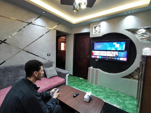 a man sitting at a table in front of a tv at شقة فندقية في بورسعيد Hotel apartment in Port Said in Port Said