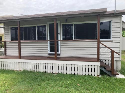 a white house with a porch with a wooden deck at Sandhills Cottage - 3 Meadow Street Keppel Sands in Emu Park