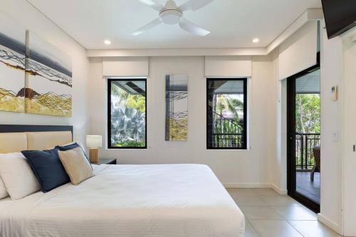 een slaapkamer met een wit bed en ramen bij Devine Rooftop Penthouse at Temple Resort in Port Douglas
