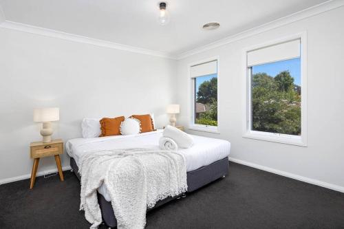 a white bedroom with a bed and two windows at Stylish Urban Getaway in the Heart of the City in Wagga Wagga