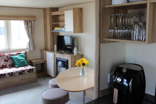 Norfolk broads caravan sleeps 8 في Belton: غرفة معيشة مع طاولة مع إناء من الزهور عليها