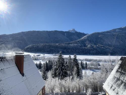 um telhado coberto de neve de um edifício com montanhas ao fundo em Das kleine Feriendorf em Karnten