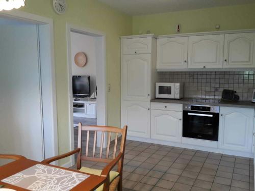 eine Küche mit weißen Schränken, einem Tisch und einer Mikrowelle in der Unterkunft Fewo Meer und Moor in Bad Zwischenahn