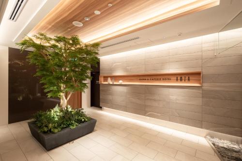 eine Lobby mit einem Baum und einem Schild an der Wand in der Unterkunft Sauna & Capsule AMZA (mens only) in Osaka