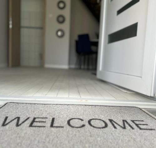 a welcome mat in front of a door with the word welcome at Aurora Apartman in Harkány