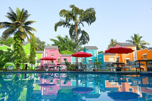 a pool with tables and umbrellas in front of buildings at Otium Goa Resort by The Oterra in Porvorim