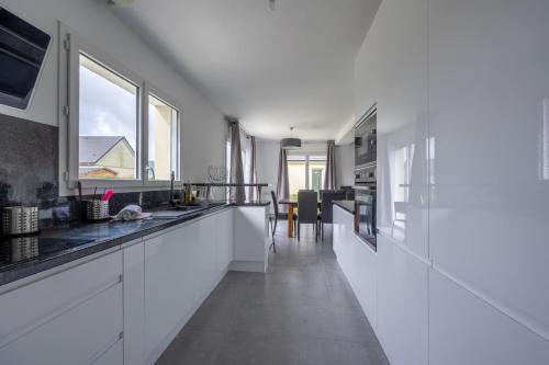 a kitchen with white cabinets and a large window at Villa Elaïa maison Familiale Omaha Beach in Saint-Laurent-sur-Mer