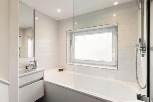 La salle de bains blanche est pourvue d'une baignoire et d'une fenêtre. dans l'établissement 1BR Chic Covent Garden Retreat, à Londres