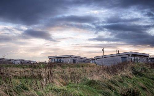 a group of buildings in a field with a cloudy sky at Jog Lodge 15 - 3 bed in Wick
