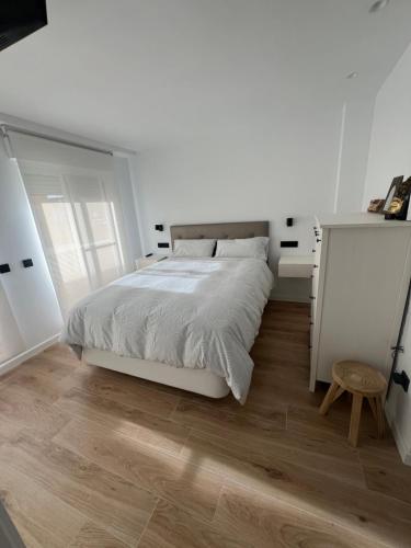 a white bedroom with a bed and a wooden floor at Como en casa! in Alfafar