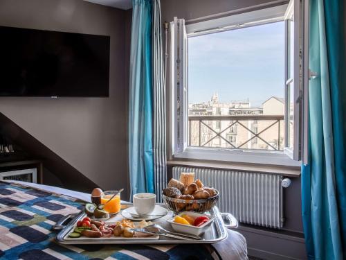 a tray of food on a bed next to a window at Mercure Paris Opera Grands Boulevards in Paris