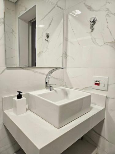 La salle de bains blanche est pourvue d'un lavabo et d'un miroir. dans l'établissement Flat na Riviera de São Lourenço com serviço de hotelaria, à Riviera de São Lourenço