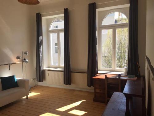 ein Wohnzimmer mit zwei großen Fenstern und einem Schreibtisch in der Unterkunft Gründerzeitzimmer mit Bad in Bonn
