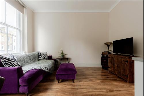 a living room with a purple couch and a tv at Spacious & stylish 1-bed flat in Primrose Hill in London