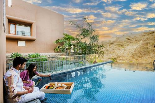 un hombre y una mujer sentados junto a una piscina en SaffronStays Moringa Wishing Tree, en Udaipur