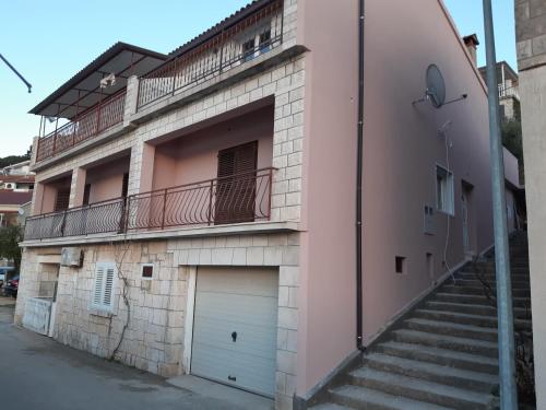 a pink building with a garage and a balcony at Apartman Stella in Smokvica