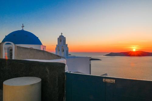 a sunset over the ocean with a church at Three Bells Suites in Firostefani