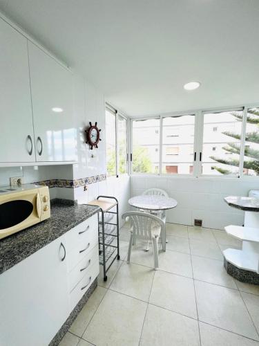 cocina con armarios blancos, mesa y mesa en Apartamento Torremar Playa, en Benicàssim