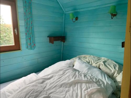 uma cama não feita num quarto azul com uma janela em Roulotte "Grain de Folie" em Waben
